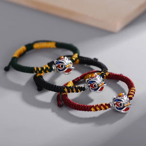 Three Lion Head Bracelet with colorful strings and metal charms on a gray surface