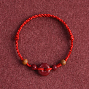 Red String Bracelet with Cinnabar Safety Buckle on a maroon background